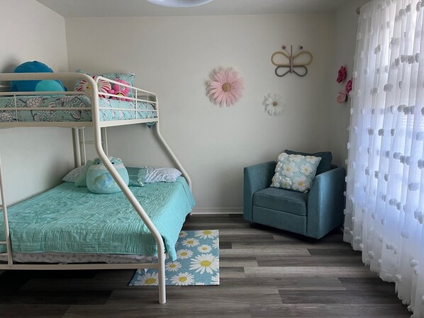 A bunk bed with a blue bedspread, a matching blue chair, and a decorative butterfly wall hanging.