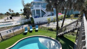 Une piscine à bord incurvé, entourée d’une terrasse en bois et d’une clôture blanche.