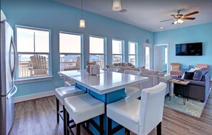 Cocina moderna con una isla central, taburetes blancos y una zona de estar con sofá y sillones.