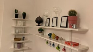 A white wall with shelves displaying various decorative items including potted plants, framed pictures, and colorful ceramic mugs. - SUMMER WITH ME😁 (Bari)