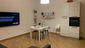A modern living room with a flat-screen TV, a dining table with chairs, a white cabinet, and a hanging light fixture. - SUMMER WITH ME😁 (Bari)