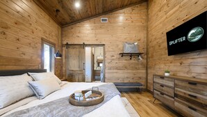 Un dormitorio tipo cabaña de madera con una cama, un televisor montado en la pared y un aparador de madera.