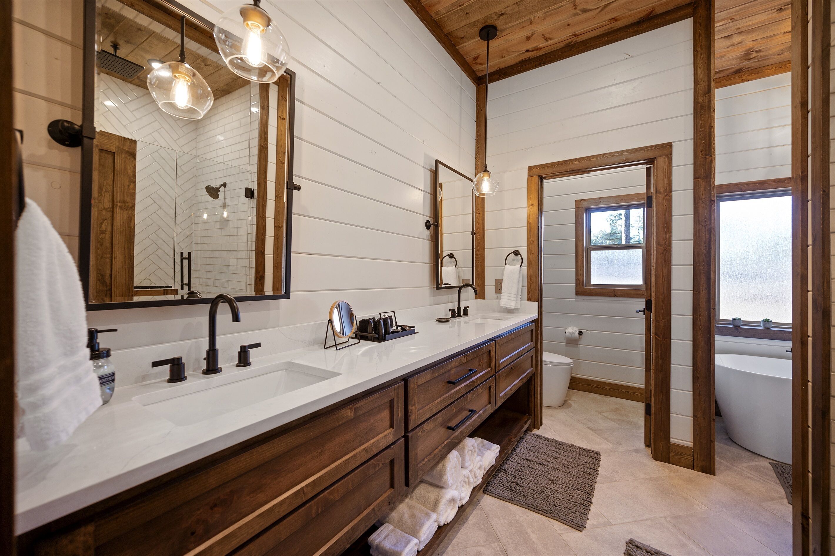 Un baño moderno con tocador de madera, dos lavamanos, un espejo grande y una bañera.