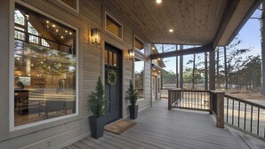 Una terraza de madera con zona cubierta, ventanas grandes y una puerta decorada con un adorno navideño.