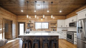 Cocina moderna con una isla central, taburetes de bar, electrodomésticos de acero inoxidable y paneles de madera.