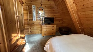 Un dormitorio acogedor en el ático, con paredes de madera, una cama, un aparador, un espejo y un televisor.