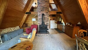 Un dormitorio tipo loft acogedor con techo inclinado, paredes de madera, chimenea integrada, kitchenette y zona de estar con sofá y sillones.