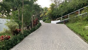 Un chemin pavé, bordé d’une rambarde blanche d’un côté et d’une végétation luxuriante de l’autre.