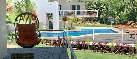 Une maison moderne avec une piscine, un fauteuil suspendu et une terrasse.