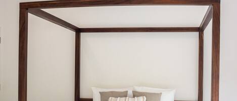 Ein Bett mit Baldachin, ausgestattet mit weißer Bettwäsche und roten Blumen, ein Holz-Kopfteil und ein Deckenventilator.