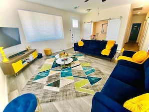 A living room with a large TV, a sofa, a coffee table, and a patterned rug.