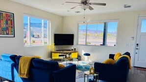 A living room with a blue sofa, a yellow lamp, and a TV. - Kickin' It on Kindra! Modern 3 Bedroom New Build! (Cottonwood)