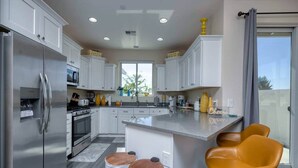A modern kitchen with white cabinets, stainless steel appliances, and a central island with stools. - Kickin' It on Kindra! Modern 3 Bedroom New Build! (Cottonwood)