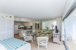 Ein kompakter Wohnraum mit Küchenzeile, einem Essbereich mit Rattanmöbeln und einem Schlafzimmer mit Bett und Schreibtisch.