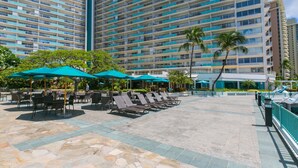 A hotel with a large outdoor pool area, multiple lounge chairs, and umbrellas.