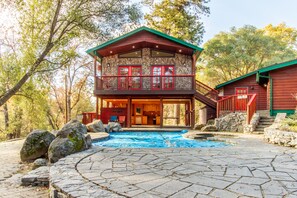 Uma pousada de dois andares com fachada de pedra, piscina e varanda vermelha.