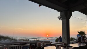 A beachside bar with a view of the sunset over the ocean.