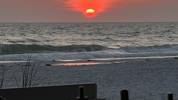 A sunset over the ocean with waves approaching the shore.