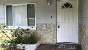 A house with a white door, a stone wall, and a tiled porch.