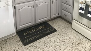 A kitchen with white cabinets, a stainless steel sink, a microwave, and a stove. There is a welcome mat with "friends & family" written on it.