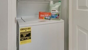 Eine kompakte Waschmaschine und Trockner-Kombination mit ENERGYGUIDE-Etikett, eine Flasche Bounce-Waschmittel und eine Flasche Flüssigwaschmittel oben drauf.