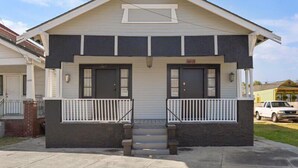 A two-story house with a front porch, a garage, and a small driveway. - Fab Studio | Walk to Food and Music | Pet Friendly (New Orleans)