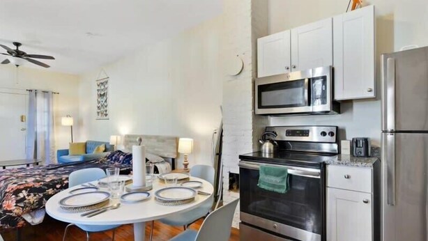 A modern kitchen with stainless steel appliances, a dining area with a round table and chairs, and a living area with a sofa and a ceiling fan. - Fab Studio | Walk to Food and Music | Pet Friendly (New Orleans)