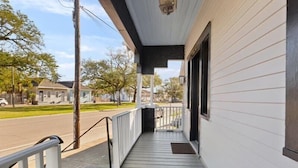 A covered porch with a white railing, a black door, and a small window. - Fab Studio | Walk to Food and Music | Pet Friendly (New Orleans)
