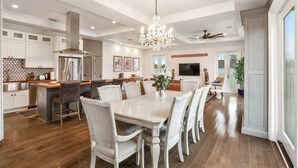 A spacious kitchen with a dining area, wooden flooring, and a chandelier.