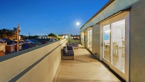 A rooftop terrace with a wooden deck, outdoor seating, and large sliding glass doors leading to an interior dining area.