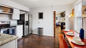 A modern kitchen with stainless steel appliances, a wooden bench, and a dining area with white plates.