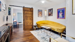 A living room with a yellow sofa, a coffee table, a floor lamp, and a wooden door.