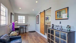 A spacious living area with a dark wooden floor, a black leather sofa, a dining table with chairs, and a sliding barn door leading to another room. - Charming Central 2BR | Courtyard | Pet Friendly (New Orleans)