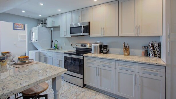 A modern kitchen with white cabinets, a granite countertop, stainless steel appliances, and a dining area with a table and chairs. - Charming Central 2BR | Courtyard | Pet Friendly (New Orleans)