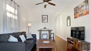 A living room with a sofa, coffee table, TV stand, and fireplace. - 2BR Steps to Music + Food | Pet Friendly (New Orleans)