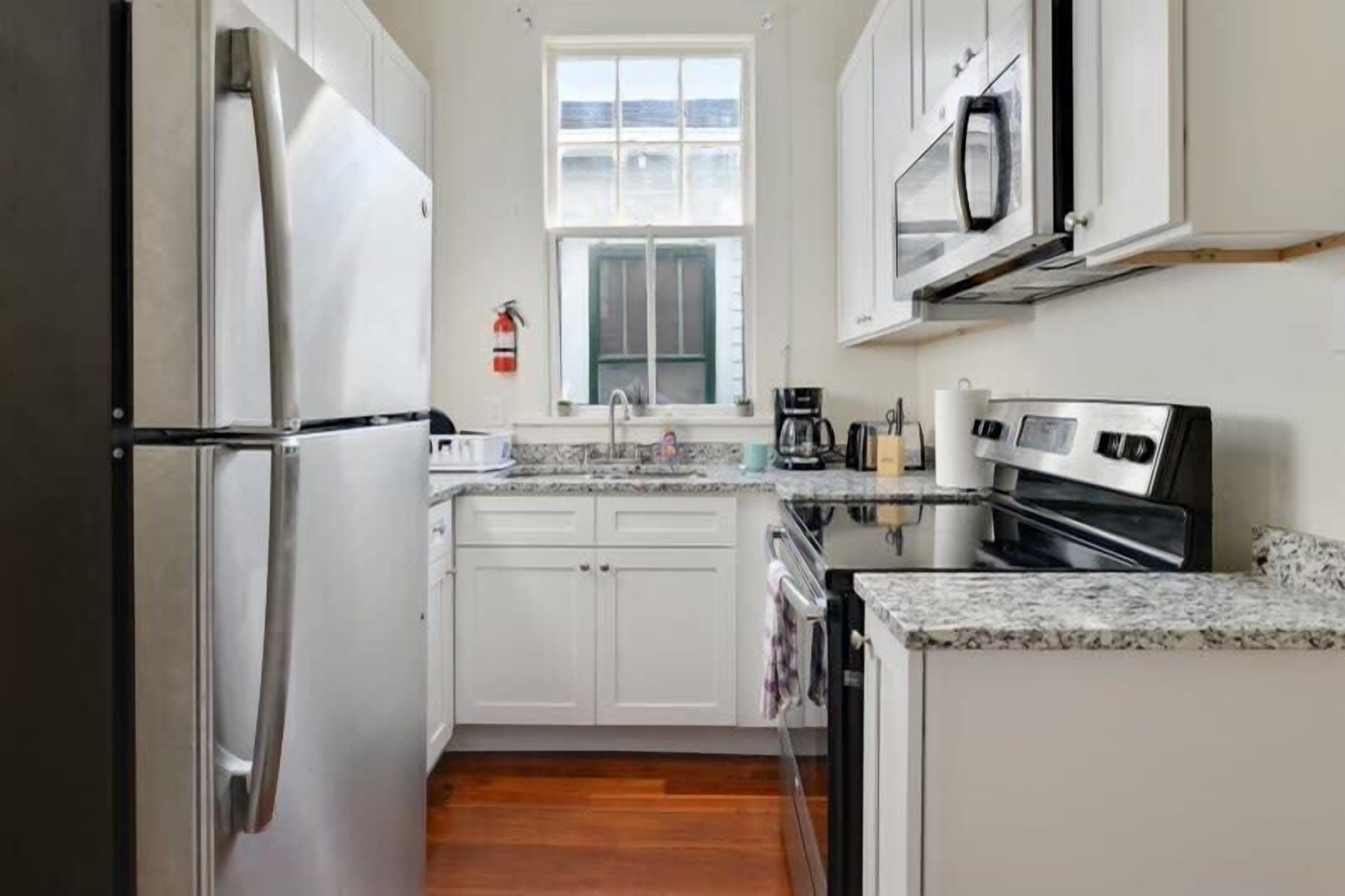 Una cocina compacta con armarios blancos, un refrigerador de acero inoxidable, un microondas y una cafetera.