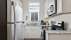 A compact kitchen with white cabinets, a stainless steel refrigerator, a microwave, and a coffee maker. - 2BR Steps to Music + Food | Pet Friendly (New Orleans)