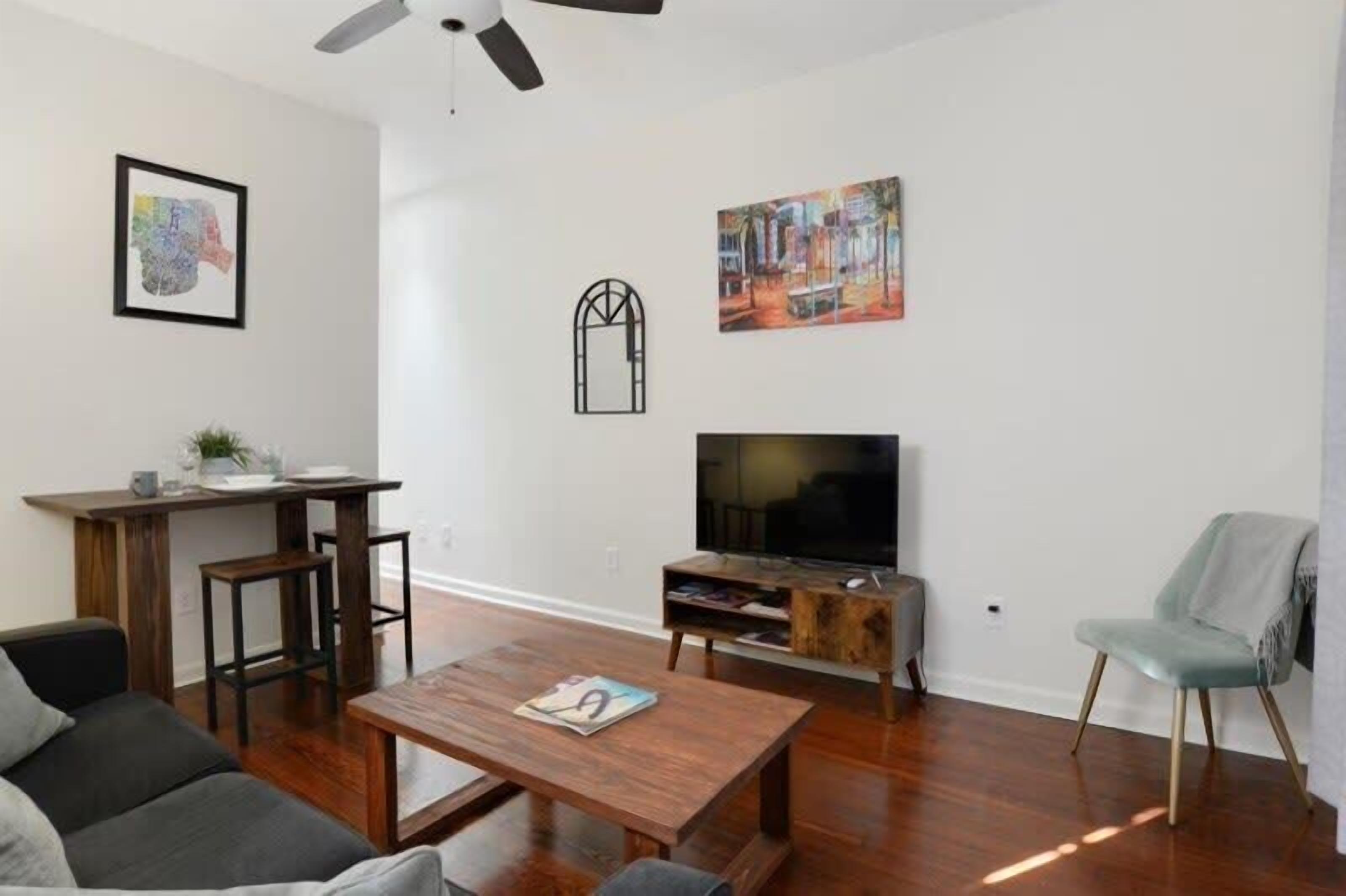 A modern living room with a wooden floor, a TV, a coffee table, a sofa, a chair, and a dining area with a table and chairs.
