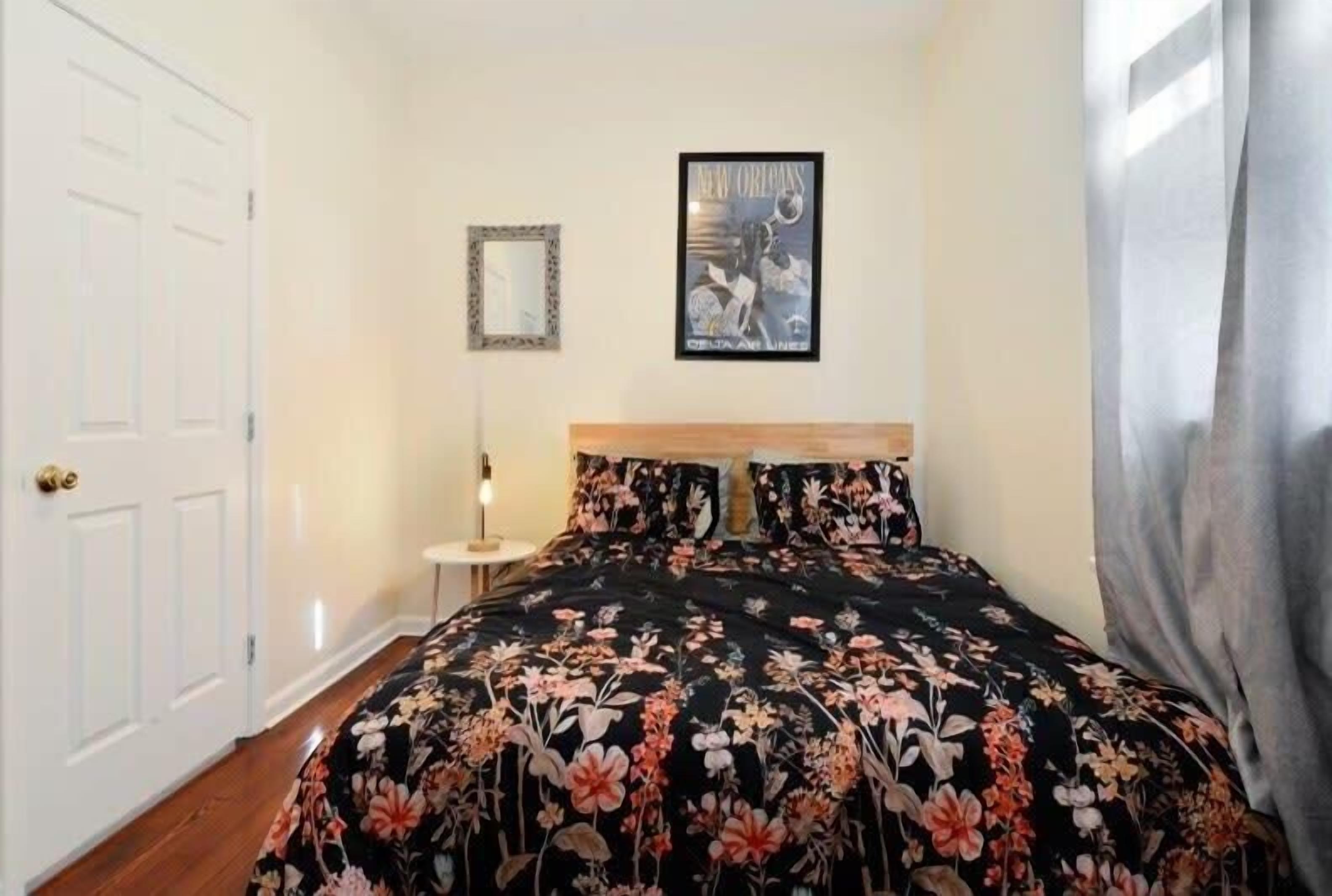 Une chambre à coucher avec une couvre-lit à motifs floraux, un tableau encadré au mur et une porte blanche.