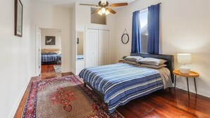 A bedroom with a bed, a ceiling fan, a nightstand, a rug, and a window with curtains.