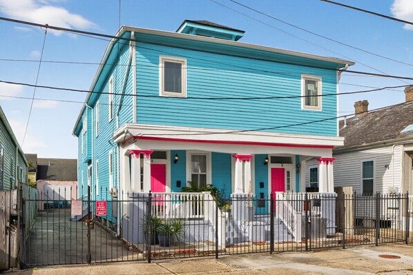 Uma casa de dois andares com fachada azul vibrante, porta vermelha e corrimão de varanda branco.