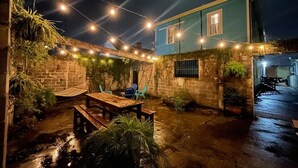 A covered outdoor patio with a wooden table and chairs, string lights, and potted plants.