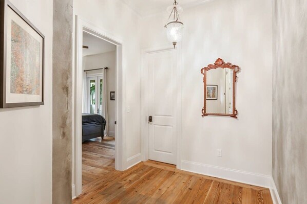 A hallway with wooden flooring, a white door, and a mirror on the wall.