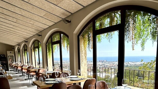A restaurant with a terrace overlooking a cityscape. Tables are set with plates, glasses, and cutlery.