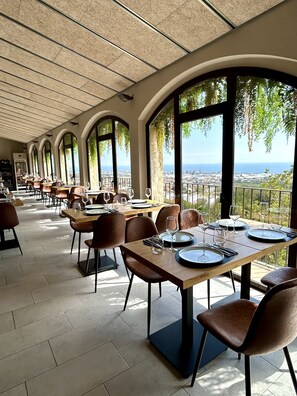 A restaurant with a terrace overlooking a cityscape. Tables are set with plates, glasses, and cutlery.