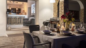 An outdoor dining area with a stone wall, a view into the kitchen, and a cozy seating arrangement.