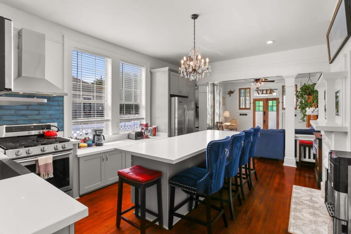 A modern kitchen with a central island, bar stools, and a chandelier.