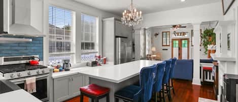 A modern kitchen with a central island, bar stools, and a chandelier.
