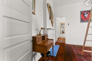 Een kamer met een houten bureau, een blauwe mat op de vloer, een rood gestreept tapijt en een ladder tegen de muur.