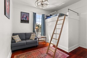 Een kamer met een bank, een ladder, een raam met gordijnen en een poster aan de muur.